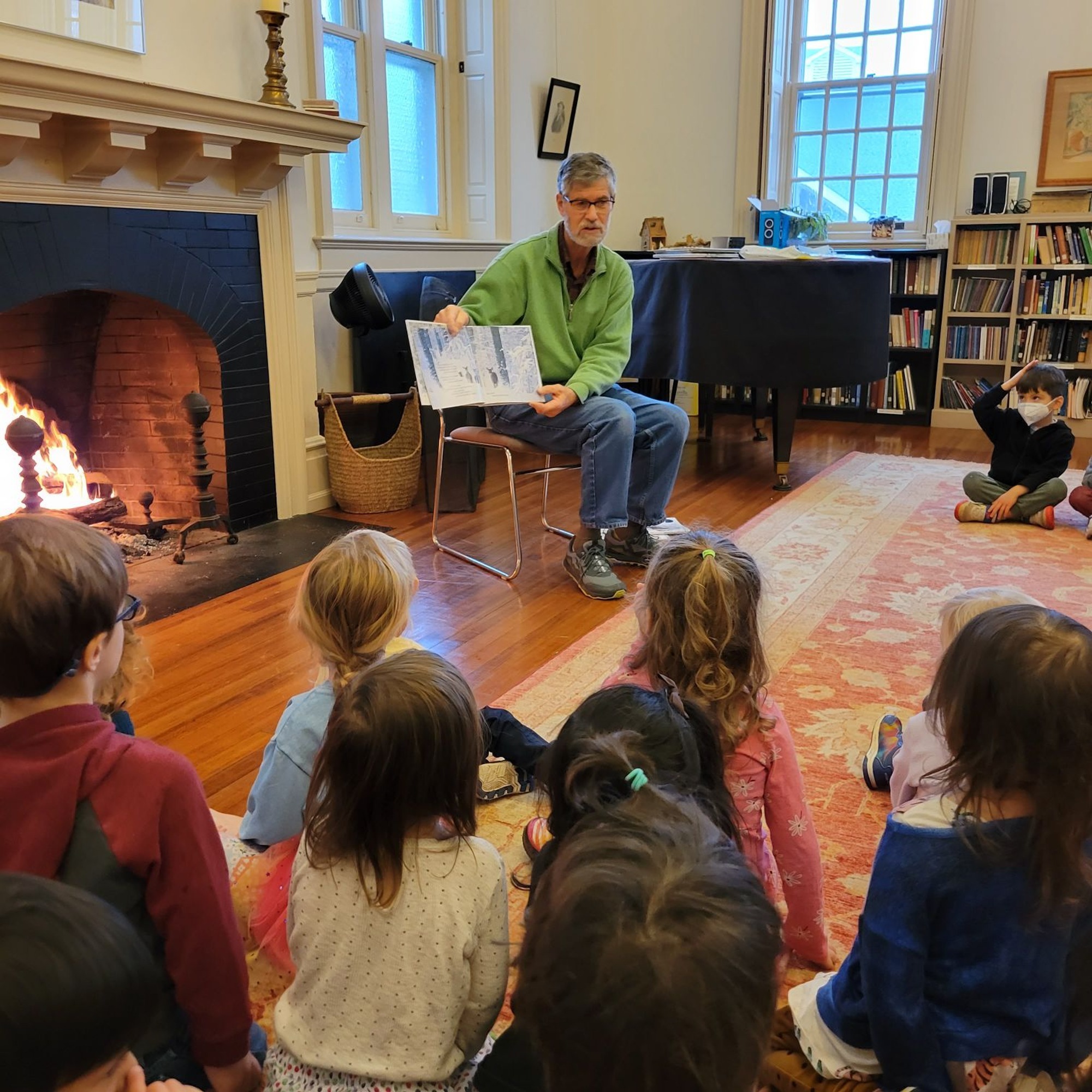 Dick Lytton is reading to children from Friends School Haverford, enjoying the warmth from the fireplace in the Forum Room. 
